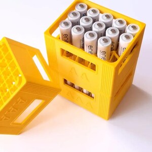 May include: A yellow plastic container filled with AAA batteries. The container is open, revealing the batteries inside. The batteries are cylindrical with silver tops and white bodies. The container is on a white surface.