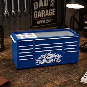 May include: A blue toolbox-shaped desk organizer with white accents and the text "Dad's Garage." The organizer has a section for small items and a larger compartment. A black mug with the text "Fueled by Coffee Built by Dad" is also visible.