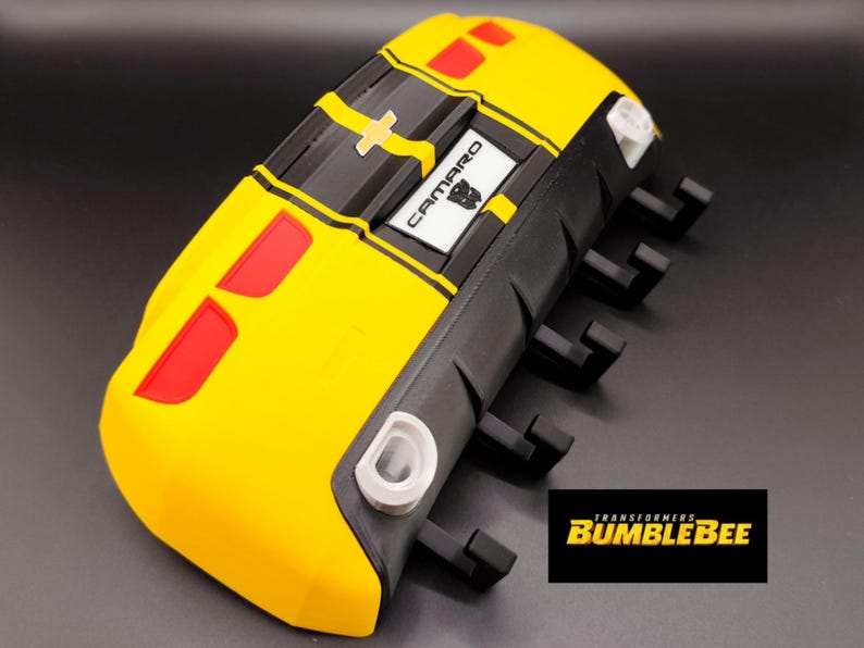Puede incluir: Un modelo Bumblebee Camaro amarillo y negro con detalles en rojo. El modelo presenta la palabra "Camaro" en un rect&aacute;ngulo blanco y el logotipo de Transformers. El modelo tiene un dise&ntilde;o detallado y est&aacute; sobre un fondo oscuro.
