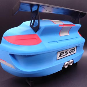 K&ouml;nnte beinhalten: Ein hellblaues Modellauto mit einem schwarzen Spoiler. Das Auto hat rote R&uuml;cklichter und silberne und rote Streifen. Das Nummernschild lautet "RS 4.0". Das Auto hat drei wei&szlig;e Auspuffrohre.