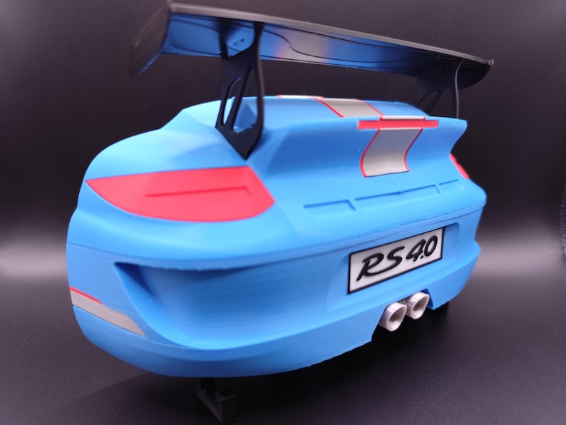 K&ouml;nnte beinhalten: Ein hellblaues Modellauto mit einem schwarzen Spoiler. Das Auto hat rote R&uuml;cklichter und silberne und rote Streifen. Das Nummernschild lautet "RS 4.0". Das Auto hat drei wei&szlig;e Auspuffrohre.