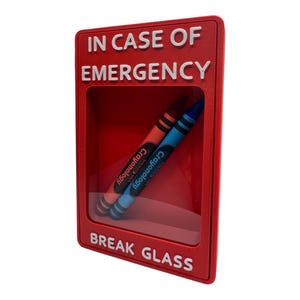May include: A rectangular red plastic wall-mounted display case with a clear front panel. The text IN CASE OF EMERGENCY and BREAK GLASS is embossed in white. Inside the case are two Crayonology crayons, one red and one blue, positioned diagonally.