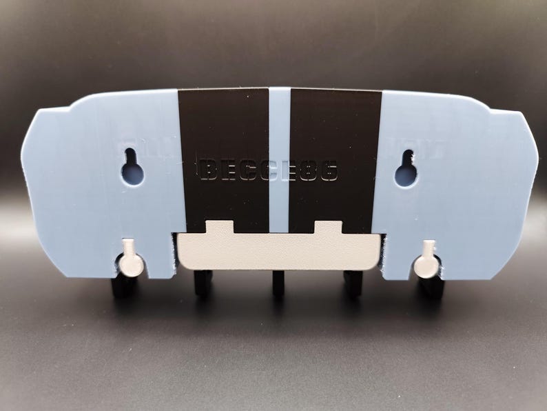 K&ouml;nnte beinhalten: Hellblauer, wandmontierter Schl&uuml;sselhalter mit schwarzen vertikalen Streifen und dem Text "BECESS6". Der Schl&uuml;sselhalter hat eine wei&szlig;e Basis und vier schwarze Schl&uuml;sselhaken. Zwei L&ouml;cher sind zur Montage sichtbar.