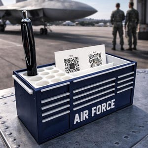 May include: A navy blue desk organizer with the words "AIR FORCE" in white. The organizer has a pen holder, a slot for business cards, and a black pen. A military jet is in the background.