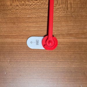 May include: A red 3D-printed object with a circular design and a stem, attached to a white, oval-shaped piece with the "3M" logo and an arrow. The object is set against a wooden surface.