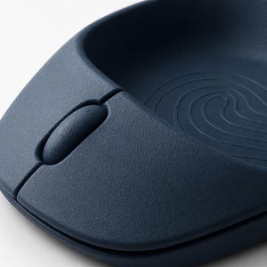 Op de afbeelding: Close-up van een marineblauwe ergonomische computermuis. De muis heeft een getextureerd oppervlak en een scrollwiel. Het ontwerp omvat een gebogen inkeping voor de hand en een golfachtig patroon.