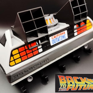 Pode incluir: Modelo da m&aacute;quina do tempo DeLorean do filme "Back to the Future". O carro &eacute; branco, preto e cinza com luzes traseiras laranja e vermelhas. Possui a placa "CALIFORNIA OUTATIME" e o logotipo "Back to the Future".