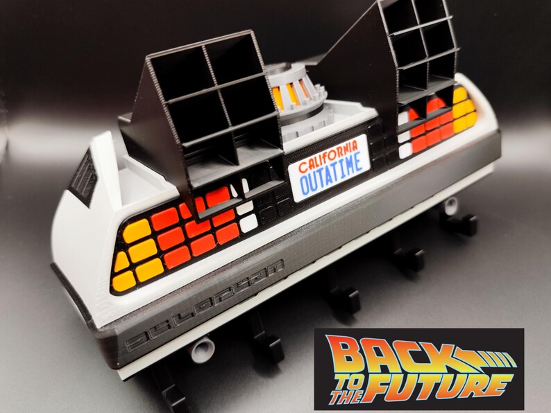 Pode incluir: Modelo da m&aacute;quina do tempo DeLorean do filme "Back to the Future". O carro &eacute; branco, preto e cinza com luzes traseiras laranja e vermelhas. Possui a placa "CALIFORNIA OUTATIME" e o logotipo "Back to the Future".