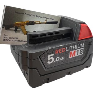 May include: A black and red Milwaukee M18 RedLithium 5.0Ah battery. The battery is on a black surface with a business card in the background.