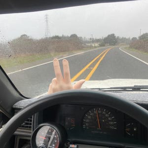 Puede incluir: Interior de un coche con un salpicadero que incluye un veloc&iacute;metro y un tac&oacute;metro. El veloc&iacute;metro indica aproximadamente 88 km/h. Una mano hace el signo de la paz. La carretera es visible a trav&eacute;s del parabrisas.