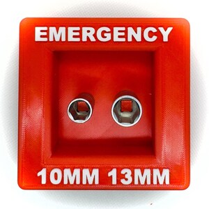 Op de afbeelding: Een rode plastic gereedschapshouder met het woord "EMERGENCY" in witte letters bovenaan en "10MM 13MM" onderaan. De houder heeft twee metalen stopcontactopeningen.
