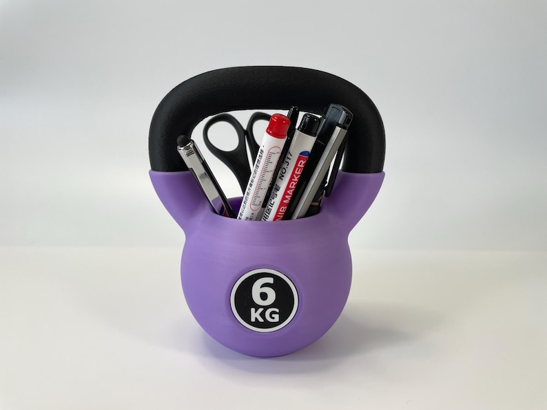 May include: A purple kettlebell-shaped desk organizer with a black handle. The organizer holds pens, markers, and scissors. The front of the organizer has a white circle with the number "6" and the letters "KG".