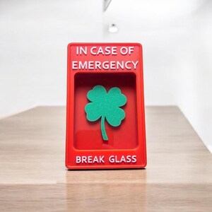 May include: Red break glass box with the text "IN CASE OF EMERGENCY" and "BREAK GLASS" in white lettering. A green four-leaf clover is visible inside the box.