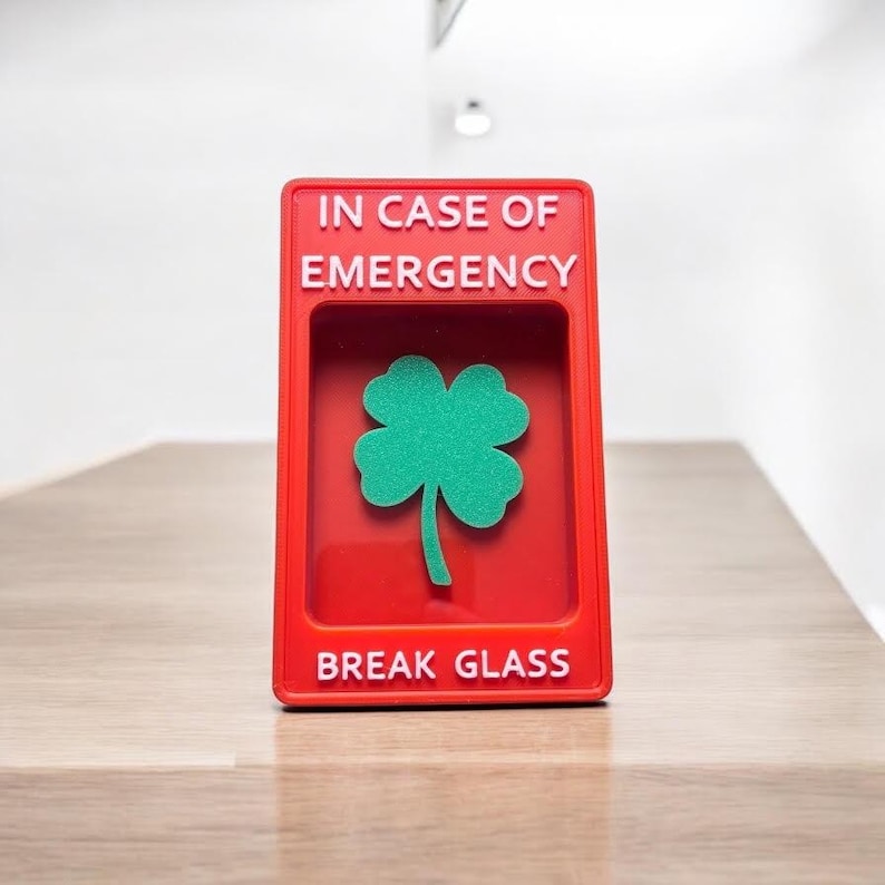 May include: Red break glass box with the text "IN CASE OF EMERGENCY" and "BREAK GLASS" in white lettering. A green four-leaf clover is visible inside the box.