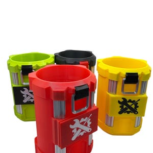 May include: A set of four cylindrical containers in lime green, black, red, and yellow. Each container features a vertical gear-like rim, silver-colored vertical accents, and a rectangular patch on the front displaying a white or black wrench and gear icon.