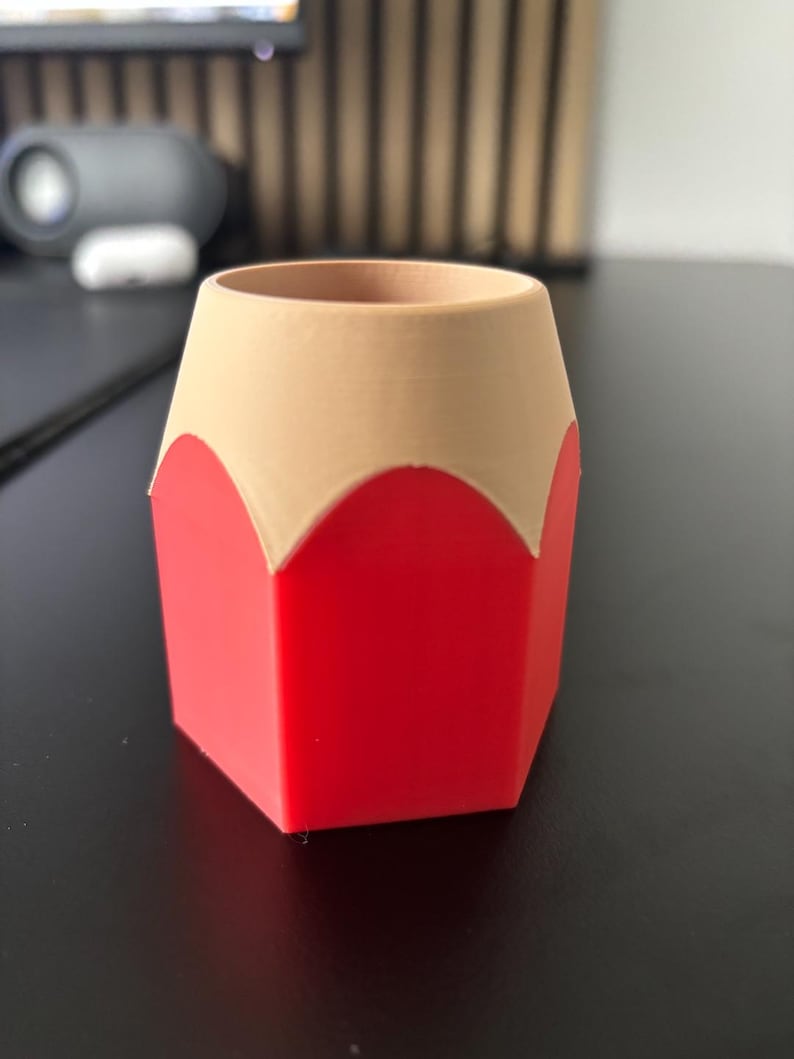 May include: A red and beige pencil-shaped desk organizer. The organizer is made of plastic and has a hexagonal base.