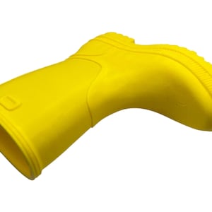 May include: A bright yellow rubber boot, angled slightly to the right, against a white background. The boot has a rounded toe, a textured sole, and a small rectangular detail near the top. The boot is likely for children.