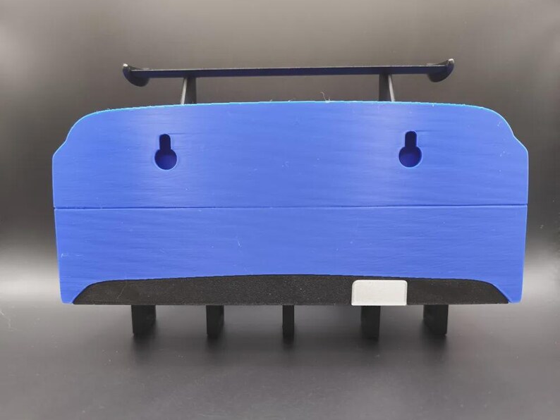 May include: A blue wall-mounted shelf with a black spoiler and black supports. The shelf has two circular holes and a black foam base. The shelf is designed to hold items and is suitable for various rooms.