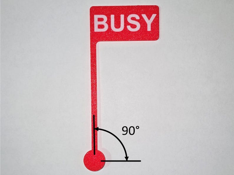 May include: A red flag-shaped sign with the word "BUSY" in white capital letters. The sign has a long, thin stem ending in a red circle. A 90-degree angle is indicated with a curved arrow.