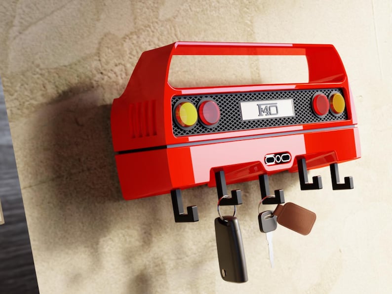 May include: A red car-shaped key holder with black hooks. The key holder has a handle and features yellow and red lights, a black grill, and the number "140". Keys hang from the hooks.