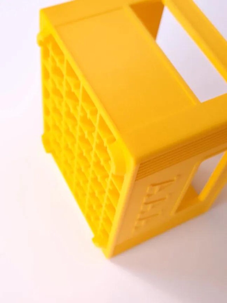 May include: A bright yellow plastic crate, featuring a grid pattern on one side. The crate is rectangular with a handle on top. The side of the crate has the letters "AAA" embossed on it.