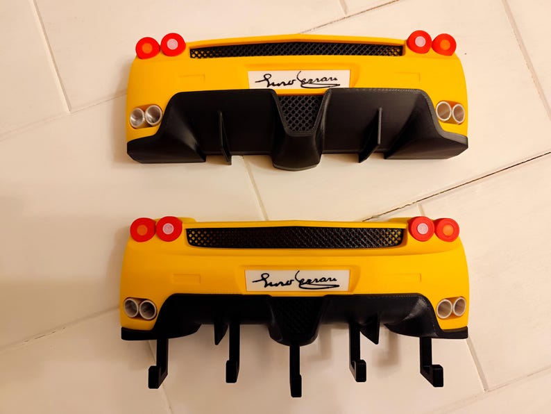 Puede incluir: Dos percheros de pared amarillos con forma de coche, detalles negros y el texto "Suno Ferrari". Cada perchero tiene luces traseras rojas y tubos de escape plateados. Los percheros est&aacute;n dise&ntilde;ados para parecerse a la parte trasera de un coche deportivo.