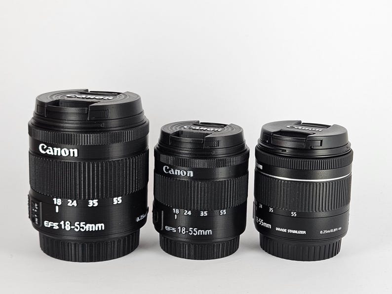 May include: Three black Canon EFS 18-55mm camera lenses. The lenses have a silver band around the middle and white markings indicating the focal length.