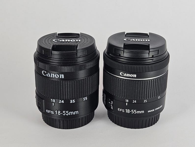 May include: Two black Canon EF-S 18-55mm camera lenses with lens caps. The lens on the left has a black finish, while the lens on the right has a silver band around the middle.