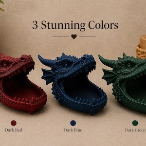 May include: Three dragon head-shaped containers in dark red, dark blue, and dark green. The containers have open mouths and are displayed on a light surface. The text "3 Stunning Colors" is above the containers.