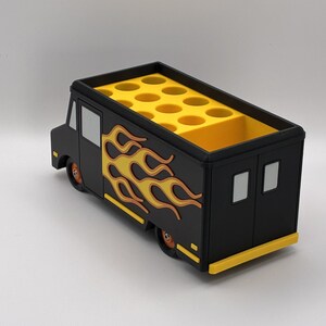 May include: A black and yellow food truck-shaped desk organizer. The organizer features a flame design on the side and a yellow interior with multiple circular compartments. The wheels and trim are also yellow.