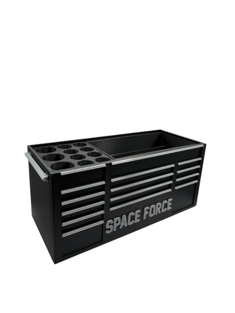 May include: Black tool chest with silver accents and the words "SPACE FORCE" in silver. The chest has multiple drawers and compartments for tool storage. It includes a section with circular holders.