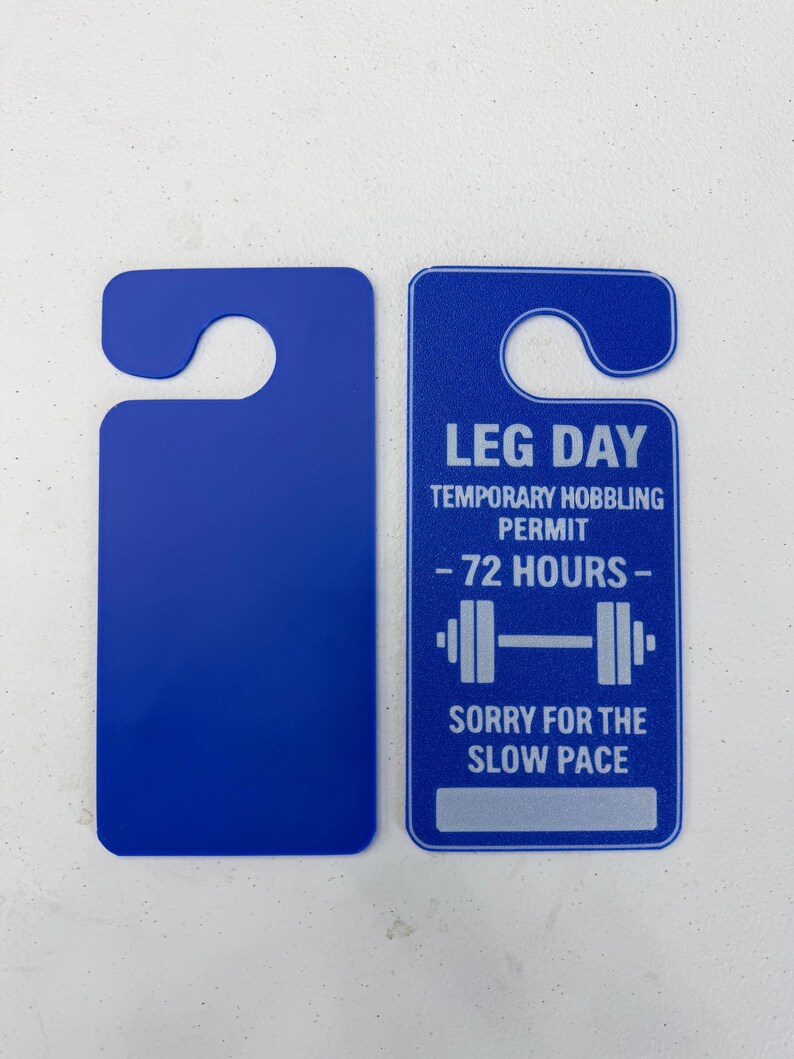 K&ouml;nnte beinhalten: Zwei blaue T&uuml;ranh&auml;nger. Einer ist leer, der andere tr&auml;gt den Text "LEG DAY TEMPORARY HOBBLING PERMIT - 72 HOURS -" mit einer Hantelgrafik und "SORRY FOR THE SLOW PACE" darunter.