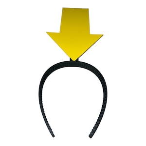 May include: A black plastic headband with a yellow arrow pointing downward. The arrow is a solid color and is attached to the top center of the headband. The headband is a simple, curved design.
