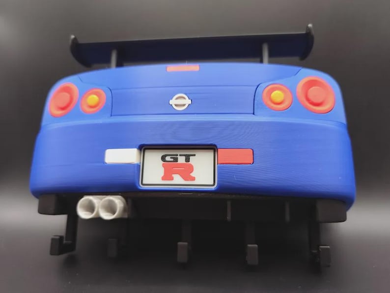 May include: A blue toy car with a rear spoiler, red and yellow taillights, and dual exhaust pipes. The car has a license plate that reads "GT" in red letters. The Nissan logo is visible.