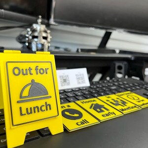 May include: A yellow sign with the text "Out for Lunch" and a graphic of a covered plate. Several yellow rectangular cards with black icons and text, including "Call", "Home", and "Meeting", are also visible.