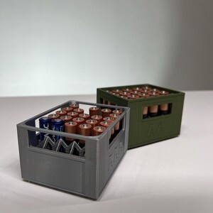 May include: Two 3D-printed battery organisers, one grey and one olive green, each filled with AA batteries. The grey organiser has a visible "AAA" label. The batteries are arranged neatly within the containers, showcasing a practical storage solution.