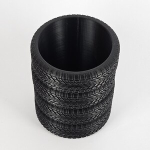 May include: A black cylindrical planter made from stacked tire treads. The planter is empty and ready to be filled with plants.