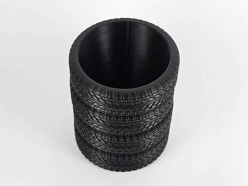 May include: A black cylindrical planter made from stacked tire treads. The planter is empty and ready to be filled with plants.