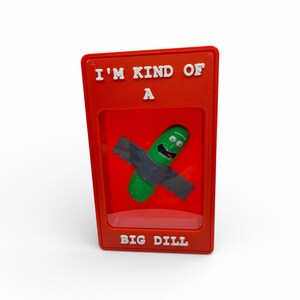 May include: A red display case with the text "I'M KIND OF A" at the top and "BIG DILL" at the bottom. Inside is a green pickle character with a gray shirt. The character has a surprised expression.