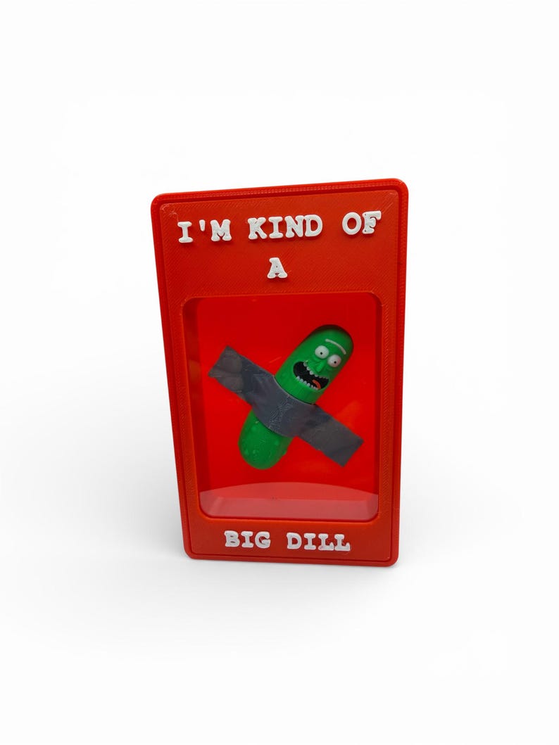 May include: A red display case with the text "I'M KIND OF A" at the top and "BIG DILL" at the bottom. Inside is a green pickle character with a gray shirt. The character has a surprised expression.