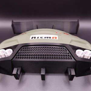 Może przedstawiać: Model 3D tylnej części samochodu z czarną kratką, rurami wydechowymi i spojlerem. Model jest gł&oacute;wnie oliwkowo-zielony i czarny, z logo "NISMO". Projekt jest szczeg&oacute;łowy i przypomina samoch&oacute;d sportowy.