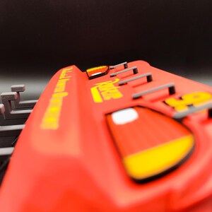 May include: A red toy car with yellow accents and the number 95. The car has the words "Radiator Springs" and "Lightning McQueen" in yellow lettering. The car has a black background.