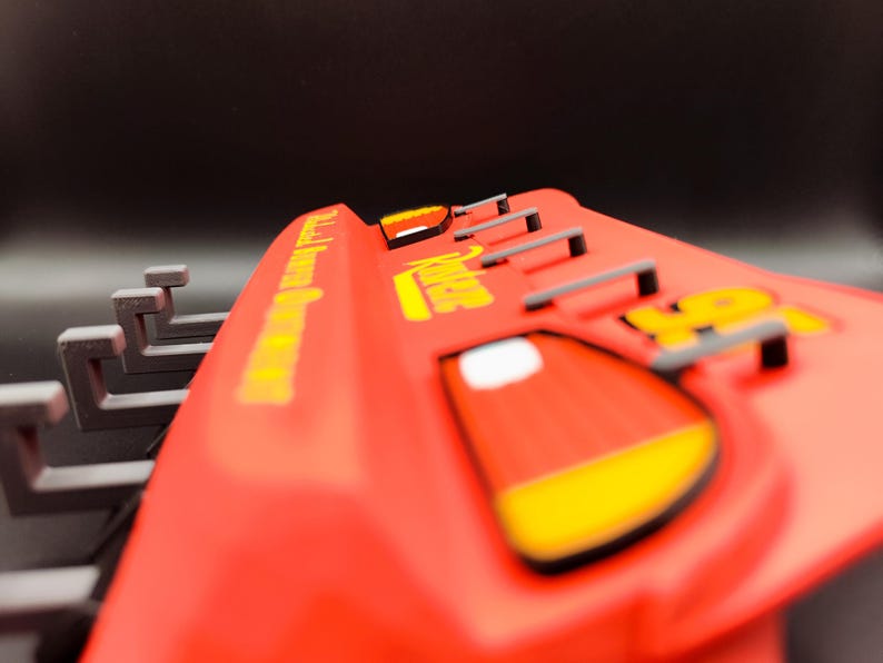 May include: A red toy car with yellow accents and the number 95. The car has the words "Radiator Springs" and "Lightning McQueen" in yellow lettering. The car has a black background.