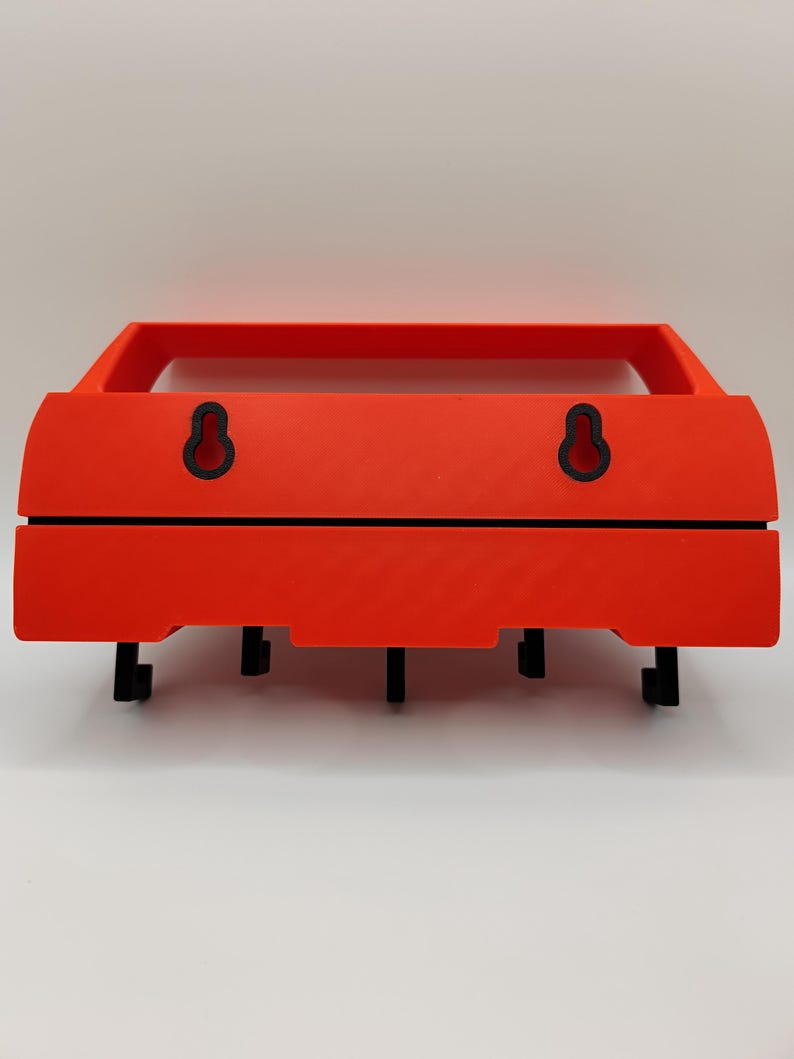 May include: A bright orange wall-mounted shelf with a rectangular frame and a lower section with four black hooks. The shelf has two black keyhole-shaped hanging mounts on the back.
