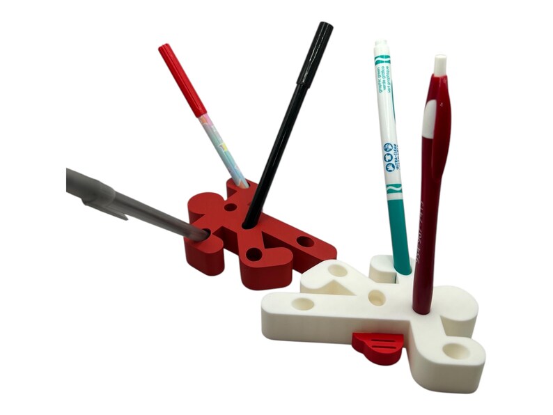 May include: Two red and white plastic pencil holders shaped like stick figures. The holders have holes for pens and pencils. There are four pens and pencils in the holders, including a black pen, a red pen, a blue pen, and a white marker.