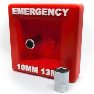 Op de afbeelding: Een rode, rechthoekige container met het woord "EMERGENCY" in witte letters. Een dopsleutel is in de container geplaatst. Onder het woord "EMERGENCY" staat de tekst "10MM 13". Een zilveren dopsleutel staat voor de container.