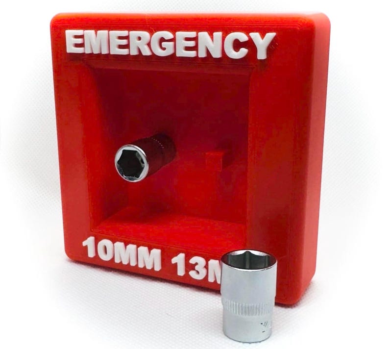 Op de afbeelding: Een rode, rechthoekige container met het woord "EMERGENCY" in witte letters. Een dopsleutel is in de container geplaatst. Onder het woord "EMERGENCY" staat de tekst "10MM 13". Een zilveren dopsleutel staat voor de container.