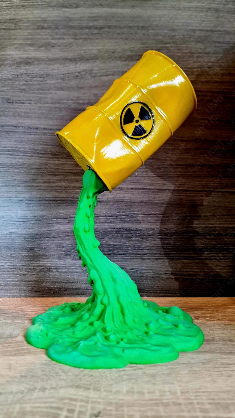 May include: A yellow barrel, marked with a black radiation symbol, is depicted pouring out a stream of bright green liquid. The liquid forms a pool at the base, creating a decorative piece.