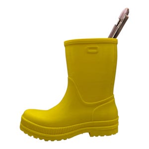 May include: A bright yellow rubber boot used as a pen holder. A silver pen is inside the boot. The boot has a textured surface and a ridged sole. The boot is approximately 8 inches tall.