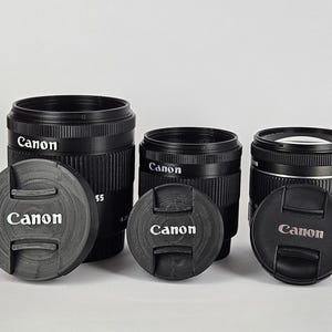 May include: Three black Canon camera lenses with lens caps. The lenses are all different sizes and have the Canon logo on them.